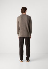 Suéter de manga larga y acanalado en color taupe, con un escote redondeado y puños ajustados, combinado con pantalones oscuros y zapatillas con suelas claras.