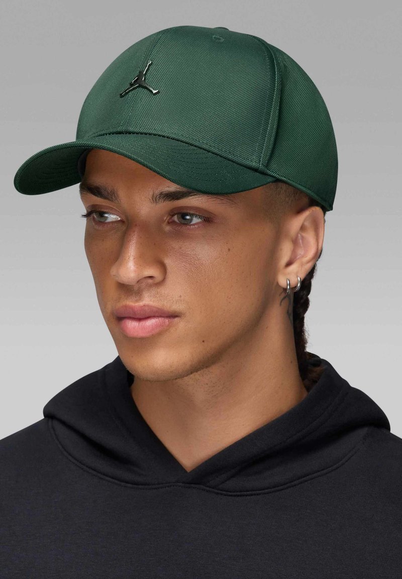 Zielona czapka bejsbolowa o strukturalnym designie, z czarnym logo Jumpman z przodu i płaskim daszkiem. Noszona z czarną bluzą z kapturem.
