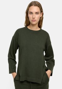 Ciemnozielony sweter z długim rękawem, z okrągłym dekoltem, bocznymi rozcięciami i luźnym krojem. Wykonany z miękkiej dzianiny. Minimalistyczny design.