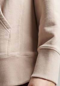 Lichtbeige sweatshirt met een getextureerd oppervlak, geribde manchetten en zichtbare naaddetails. Het materiaal lijkt zacht en casual.