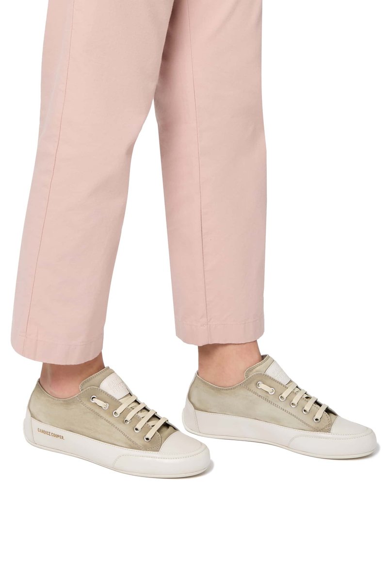 Hellbeige Sneaker mit Wildleder- und Lederdetails, runder Zehenpartie, weißer Gummisohle und beige Schnürsenkeln. Begleitet von hellrosa Hosen.