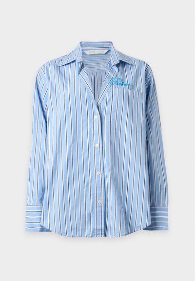 Ανοιχτό μπλε πουκάμισο με μακριά μανίκια και κάθετες λευκές και μαύρες ρίγες, τσέπη στο στήθος και μικρό κεντητό κείμενο "Palm" πάνω από την τσέπη.