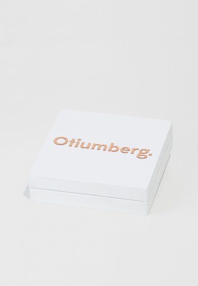 Bijela pravokutna kutija s glatkom površinom i lagano uzdignutim, reljefnim logotipom u boji bakra "Otiumberg." na vrhu.
