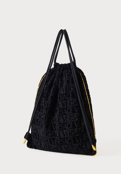 Crna velvet torbica s vezicama, s utisnutim Versace logotipom, žutim obrubom i dvostrukim crnim remenima, s mekanim, teksturiranim završetkom.