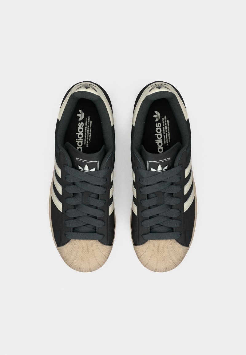 Svarta Adidas-sneakers med en beige gummitäcksko, tre beige ränder, texturerat tyg och vadderad krage.