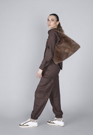 Camicia marrone con texture e pantaloni cargo con polsini elasticizzati, abbinati a una borsa in finta pelliccia marrone con una toppa logata beige, e sneaker bianche con dettagli argentati.
