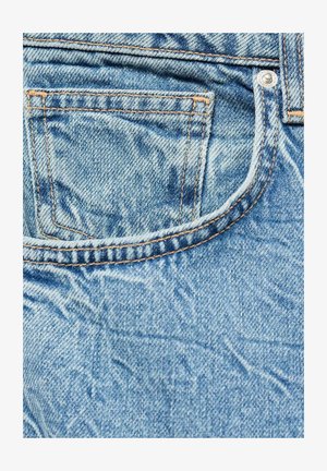 Svetlomodré džínsy s vyblednutou textúrou, majúce zadnú vrecko, kontrastné oranžové šitie a detail kovového gombíka.