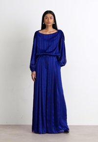 Longue robe plissée bleue avec un large col et des manches longues. Fabriquée dans un tissu brillant. Elle est dotée d'une ceinture élastique pour une silhouette ajustée.