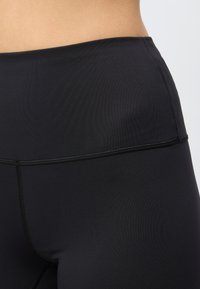 Κοντινό πλάνο της μέσης και των γοφών, που φοράει μαύρα κολάν με ψηλή μέση, εμφανείς ραφές και ομαλή υφή υφάσματος.