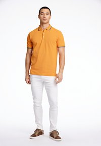Orange polo skjorta med krage, med grå detaljer på ärmarna och halsen. Kombinerad med slim fit vita byxor och bruna sneakers.