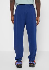 Granatowe spodnie sportowe z elastycznym pasem, luźnym krojem i zwężającymi się mankietami. Materiał wydaje się gładki z minimalnie widocznymi szwami.