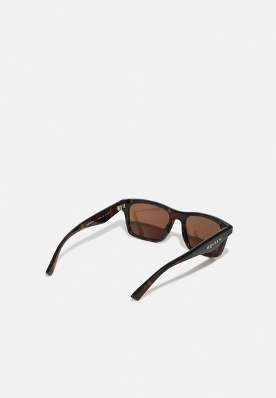 Occhiali da sole tartarugati con lenti marroni, montatura rettangolare e aste sottili. Presentano un logo discreto sul lato con dettagli metallici.