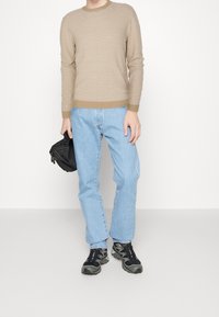 Beige randig stickad tröja med rund halsringning, matchad med ljusblå raka jeans och svarta sneakers, håller en liten svart väska.