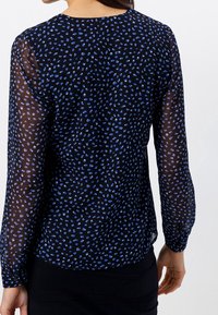Blusa nera trasparente con motivo a macchie blu, maniche lunghe, scollatura rotonda e tessuto morbido e leggero. Nessuna ferramenta o dettaglio visibile.