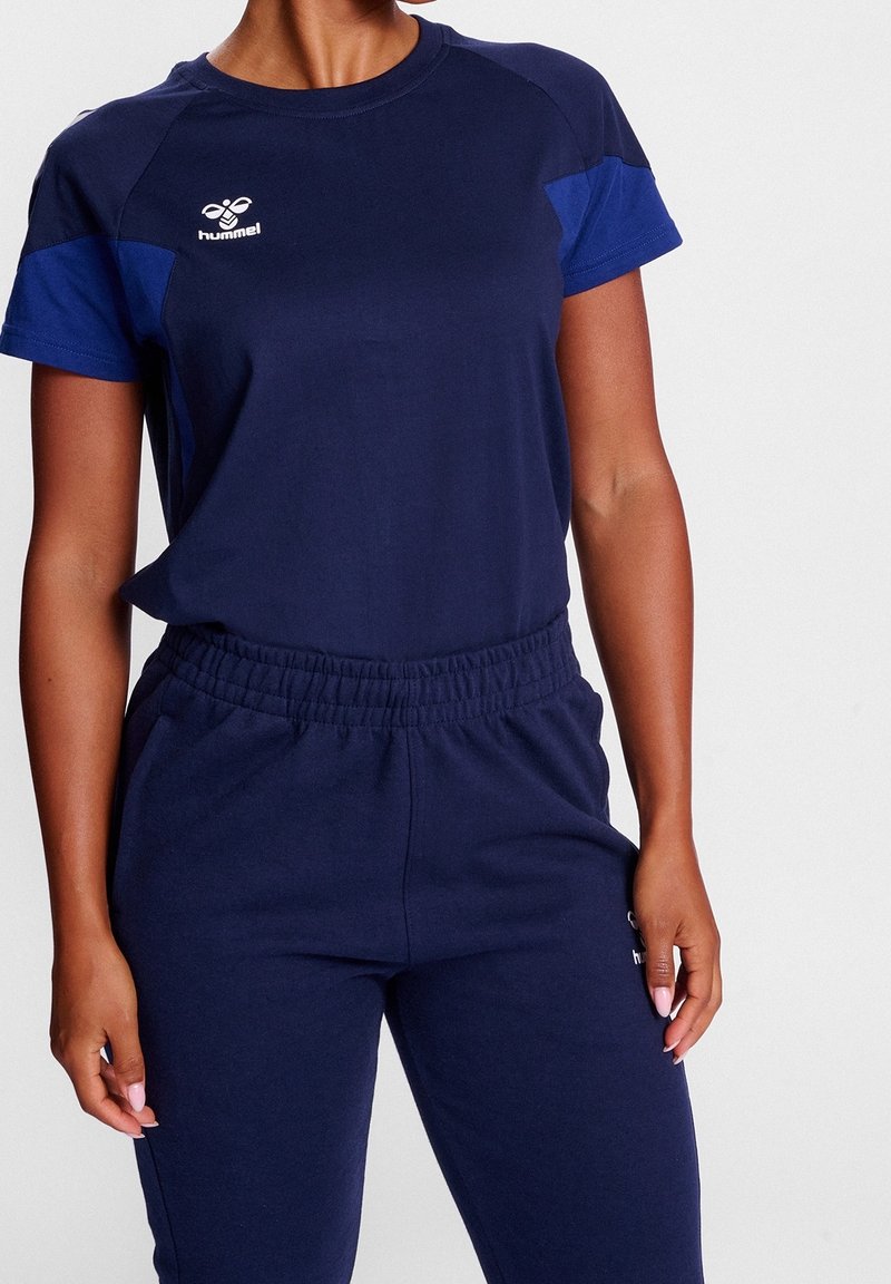 Navy blue urheiluasu, joka on valmistettu puuvillasekoitteesta; lyhythihainen paita ja yhdisteet, joissa on joustava vyötärö ja logo yksityiskohtana.