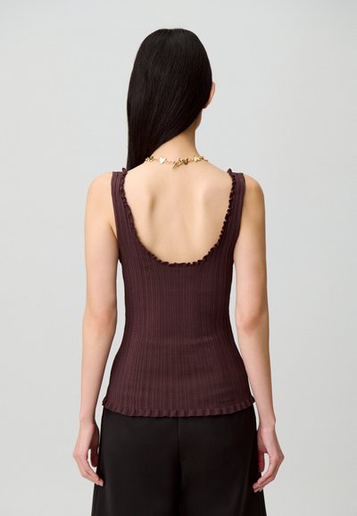 Top marrone a coste con schiena bassa e bordi arricciati. Il tessuto sembra aderente con una texture liscia. Abbinato a pantaloni neri larghi.