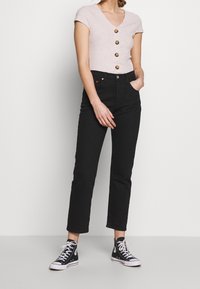 Lys pink ribbet t-shirt med korte ærmer og V-hals samt guldknapper, parret med sorte højtraljede jeans og sorte højtop sneakers.