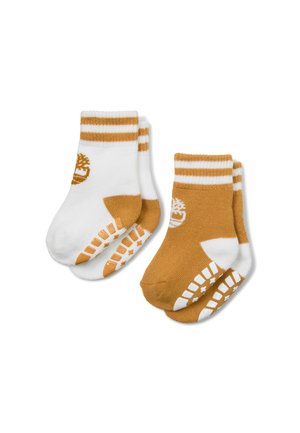 Paires de chaussettes pour tout-petits, une blanche avec des accents et un logo beige, l'autre beige avec des accents et un logo blanc, les deux avec des motifs antidérapants sur les semelles.