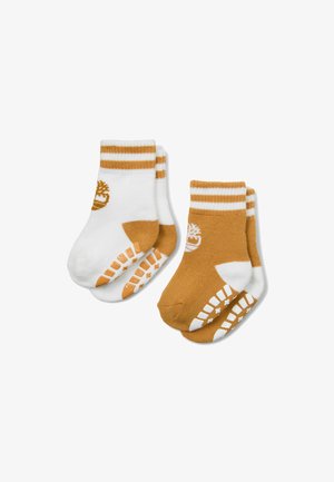 Paare von Kleinkind-Socken, eine weiße mit beigen Akzenten und Logo, eine beige mit weißen Akzenten und Logo, beide mit Grip-Mustern auf der Sohle.