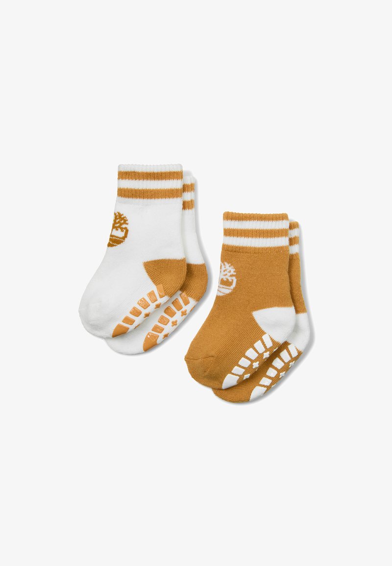 Par af børnestrømper, en hvid med brune detaljer og logo, en brun med hvide detaljer og logo, begge med skridsikre mønstre på sålerne.
