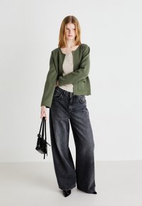 Πράσινο πλεκτό cardigan συνδυασμένο με μπεζ ριμπ κορυφή, σετάρισμα με φαρδιά μαύρα τζιν και μικρή μαύρη τσάντα. Διαθέτει μαύρα μυτερά παπούτσια.