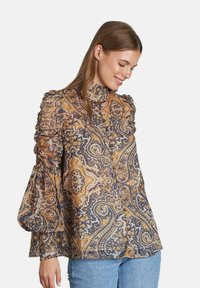 Blusa de manga larga con estampado de paisley en tonos de azul marino, dorado y crema. Hombros con volantes y mangas voluminosas, fabricada en tela ligera.