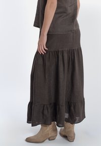 Bruine linnen maxi rok met een gerimpelde zoom, gecombineerd met beige enkellaarsjes. Glad textuur en vloeiende ontwerp met een gelaagde uitstraling.