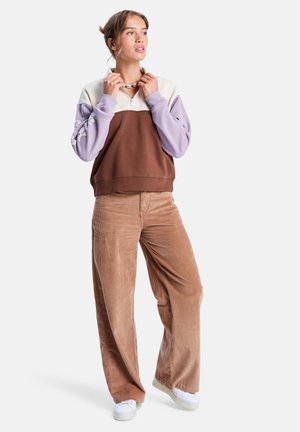 Bruin en lila kleur-geblokte pullover met een ritskraag, gecombineerd met lichtbruine corduroy wijde broek en witte sneakers.
