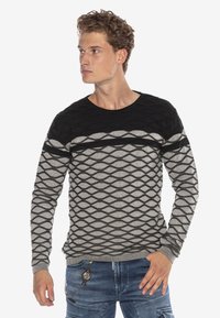 Schwarzer und grauer Langarmpullover mit einem strukturierten Rautenmuster, Rundhalsausschnitt und gerippten Bündchen; getragen mit blauen Jeans.