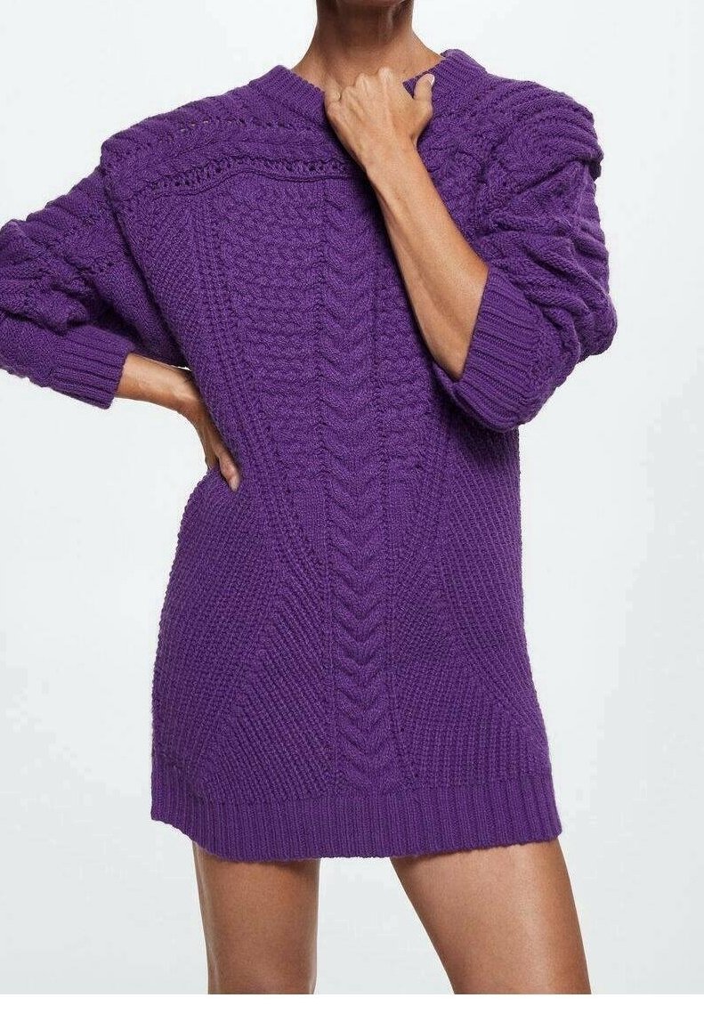 Personne portant une robe pull oversize en maille torsadée texturée de couleur violette avec des manches longues, posant avec une main sur la hanche et l'autre près du cou.