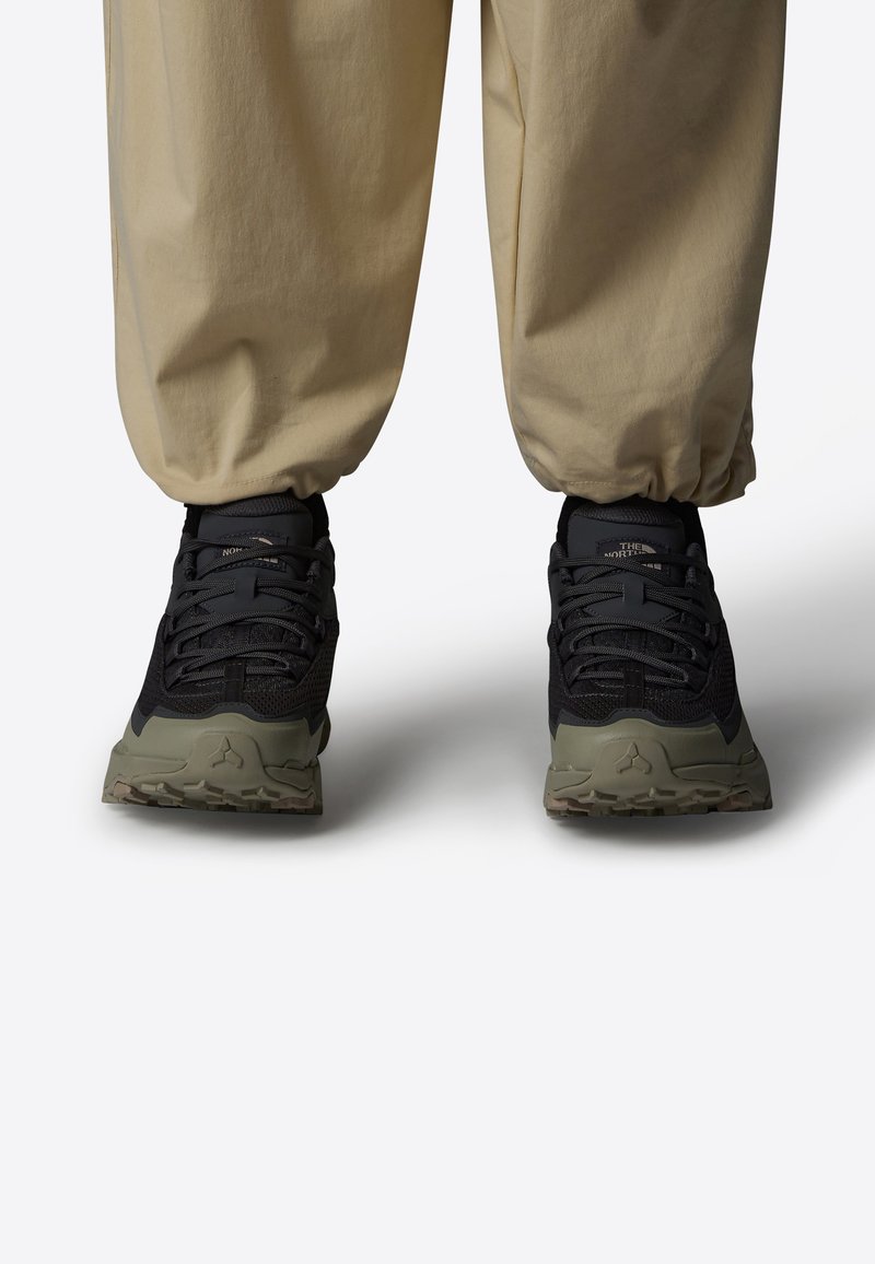 Svart mesh-sneakers med grønne detaljer og teksturerte såler. Har snøring og polstret krage, synlig merking på hælen.