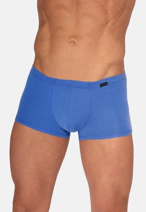 Männlicher Oberkörper in eng anliegenden blauen Boxershorts, zeigt muskulösen Bauch und Oberschenkel vor einfachem Hintergrund.