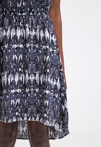 Námořnické modré šaty z jemné tkaniny, s abstraktním bílým vzorem, elastickým pasem a mírně zakřiveným lemem.