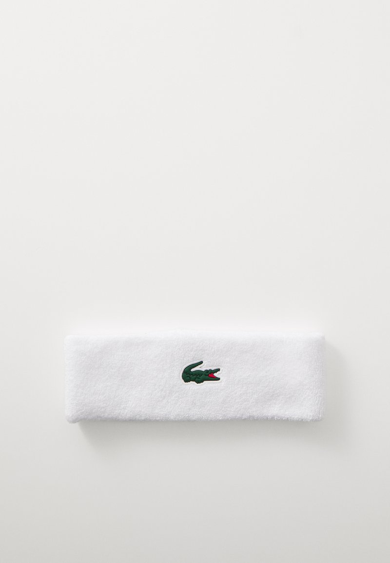 Weißes Baumwoll-Terry-Haarband mit einem grünen Krokodil-Logo und roten Akzenten in der Mitte, rechteckige Form, weiche Textur.
