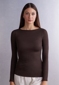 Braunes Langarmoberteil aus glattem Stoff, mit einem Bootsausschnitt und einer taillierten Silhouette. Weiße Hosen sind teilweise sichtbar.