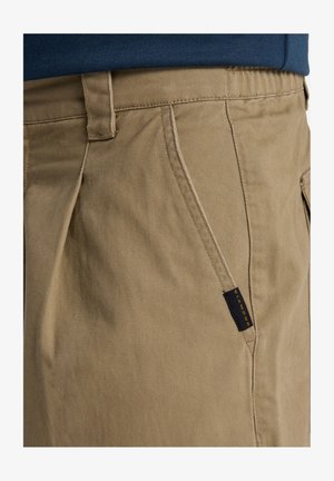 Chinos caqui con una tela suave y duradera de acabado texturizado, bolsillos laterales en ángulo y una etiqueta negra y amarilla en la cinturilla.