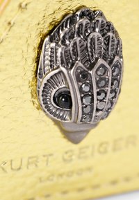 Yellow leather bag featuring a silver metallic embellishment shaped like a stylized eye with intricate detailing and black stone accents.