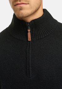 Zwart gebreid sweater met een hoge geribbelde kraag en een rits tot halverwege. Voorzien van een leren ritstrekkertje en een gestructureerd, zacht materiaal.