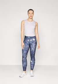 Maritimmönstrade leggings med hög midja, matchade med en ljusgrå ärmlös topp. Modellen står i vita sportskor.