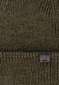 Dunkelgrüne Strickmütze mit dicker Textur, versehen mit einem schwarzen Logostick auf dem Stoff. Lässige und enge Passform für Wärme.