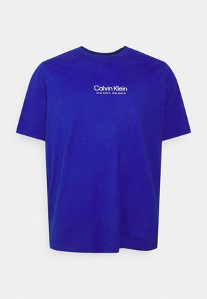 T-shirt bleu roi à manches courtes avec logo blanc "Calvin Klein" et coordonnées géographiques imprimées en petits caractères sur la poitrine.