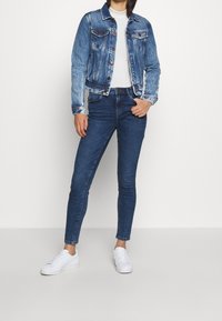 Jeansjacka i medelblått, med två bröstfickor och knappframsidan. Matchas med mörkblå skinny jeans och vita sneakers.