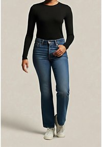 Personne portant un haut noir ajusté à manches longues associé à un jean bleu taille haute et des baskets blanches, debout devant un fond uni.