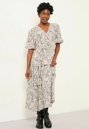 Langes, gestuftes Kleid in Hellgrau mit Blumenmuster; Puffärmel; V-Ausschnitt; getragen mit schwarzen Kampfstiefeln. Weicher Stoff mit einer lässigen Silhouette.