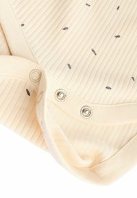 Crème ribstof met kleine donkergrijze stippen; heeft drukknoopsluitingen aan de onderkant en een zachte textuur; geschikt voor casual wear.