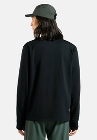 Maglietta nera a maniche lunghe con un motivo testurizzato, caratterizzata da un collo tondo e una vestibilità leggermente ampia, abbinata a pantaloni verde oliva e a un cappellino.