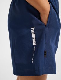 Marina idrottsshorts med en slät yta, utrustade med en sidficka, "hummel"-logotyp i vitt och en liten svart etikett med ett chevronmönster.