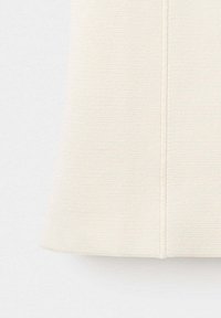 Gros plan de la partie inférieure d'un tissu texturé couleur crème avec une couture verticale au centre.