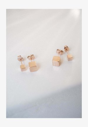 Zwei Paare roségoldene quadratische Ohrstecker, ein Paar mit größeren und das andere mit kleineren Würfeln, auf einer weißen Oberfläche dargestellt.