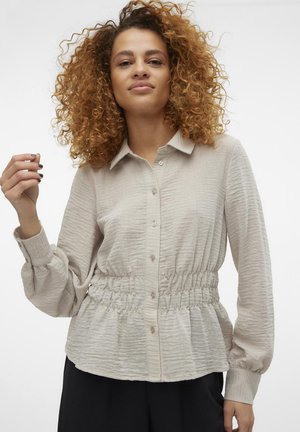 Lys beige skjorte med knapper foran og en rynket tekstur, elastisk liv for en samlet utseende; lange ermer med knappede mansjetter.